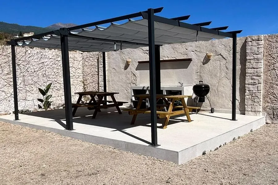 Pérgola con cocina exterior: solería cerámica y pared de roca tematizada, obra de Natural Rocks Design